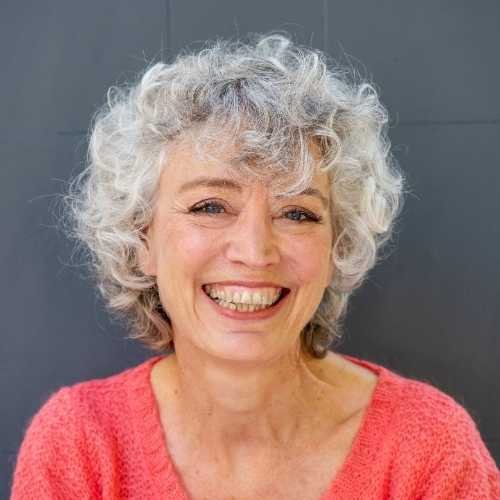 Mature aged woman, smiling, grey hair, pink jumper, headshot.