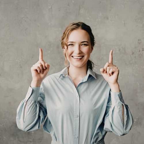 Young woman in corporate clothing, smiling, pointing to the ceiling. representing corporate counselling, EAP psychosocial safety, and workplace wellbeing services.